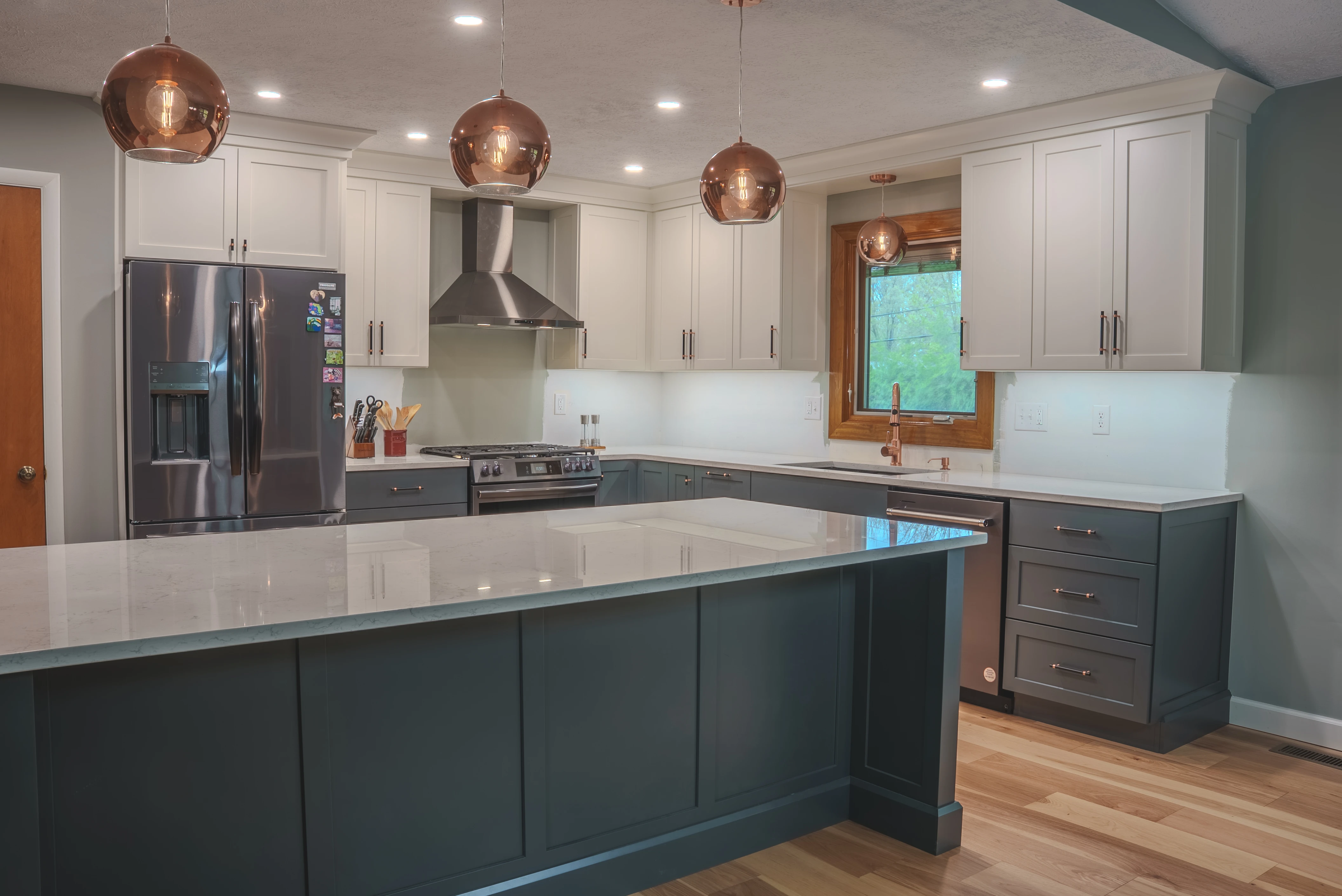 Beautiful modern kitchen remodel featuring white upper cabinets, dark lower cabinets, copper pendant lights, and white quartz countertops